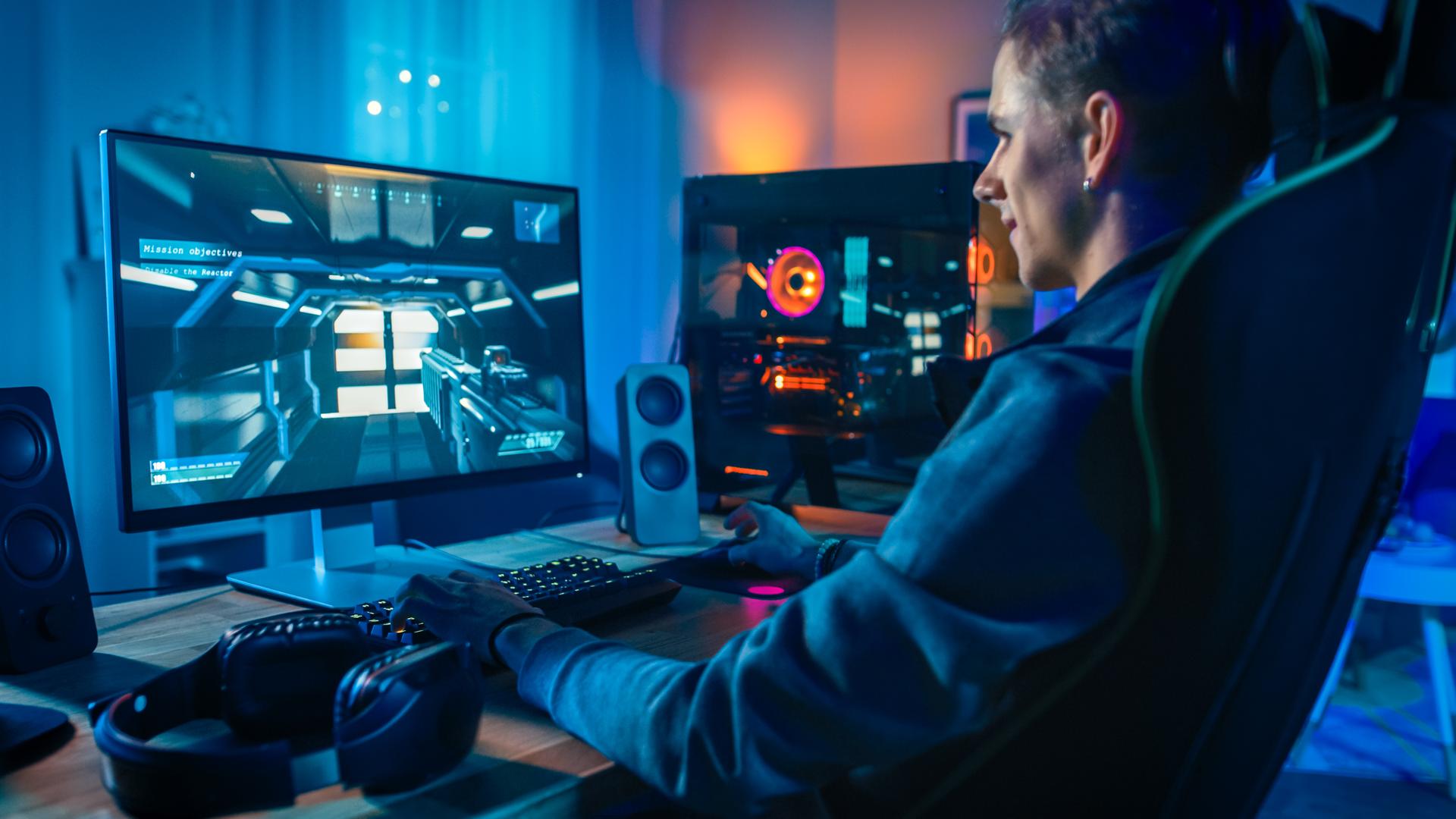 Happy Gamer Playing First-Person Shooter Online Video Game on His Powerful Personal Computer. Room and PC have Colorful Neon Led Lights. Cozy Evening at Home.