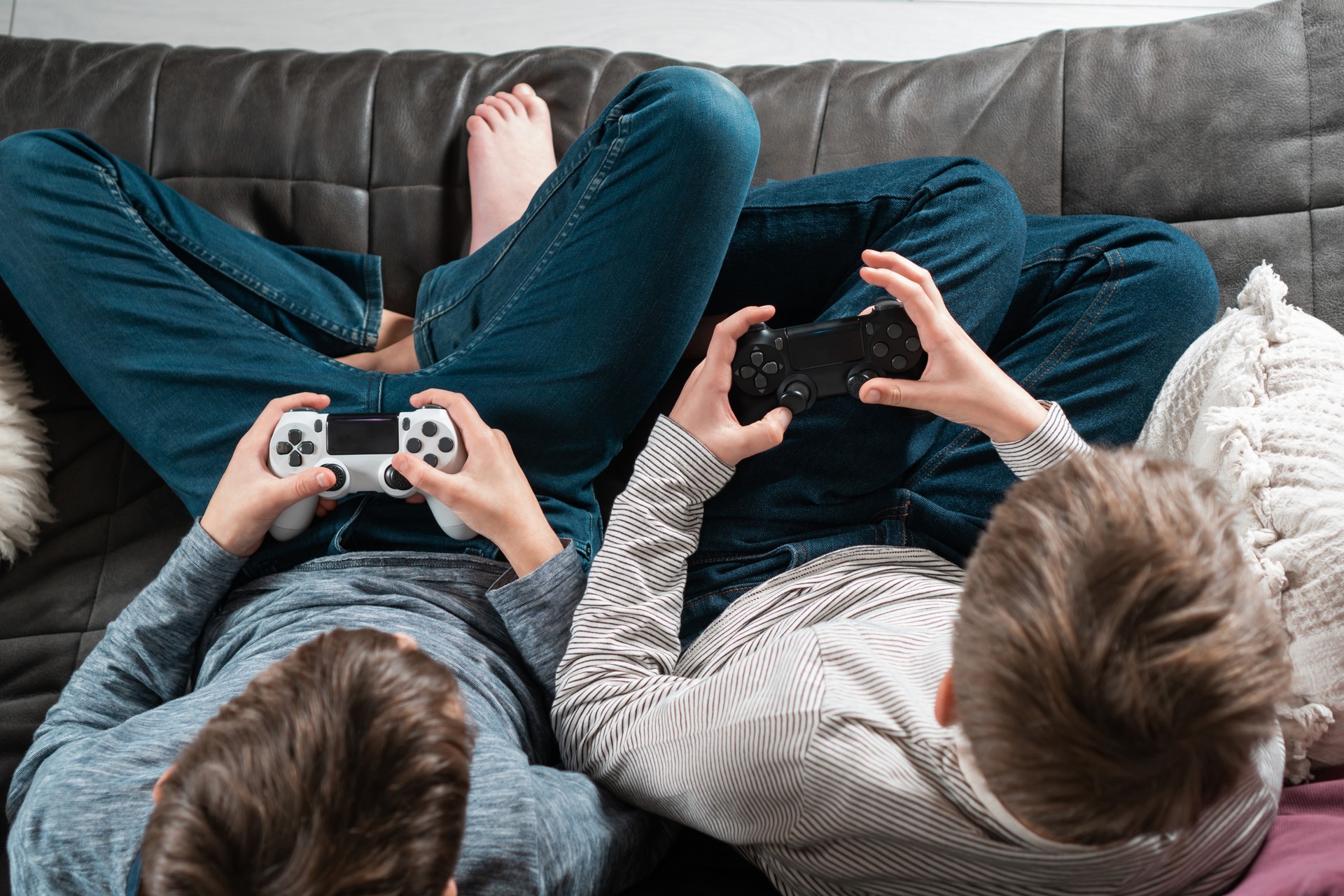 Top view of two teenage boys children sitting on sofa at home, holding gaming controller joystick, playing videogames.